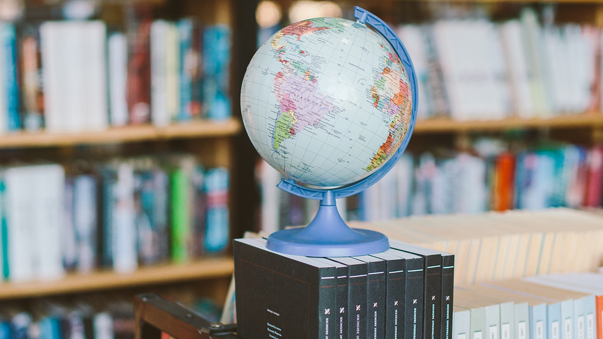 a miniature globe on a row of books in a library